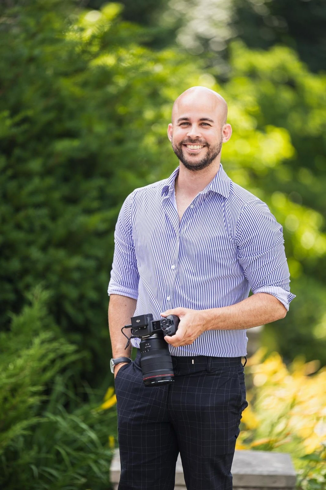 Harold Rivero, photographer, smiling and holding his camera outdoors