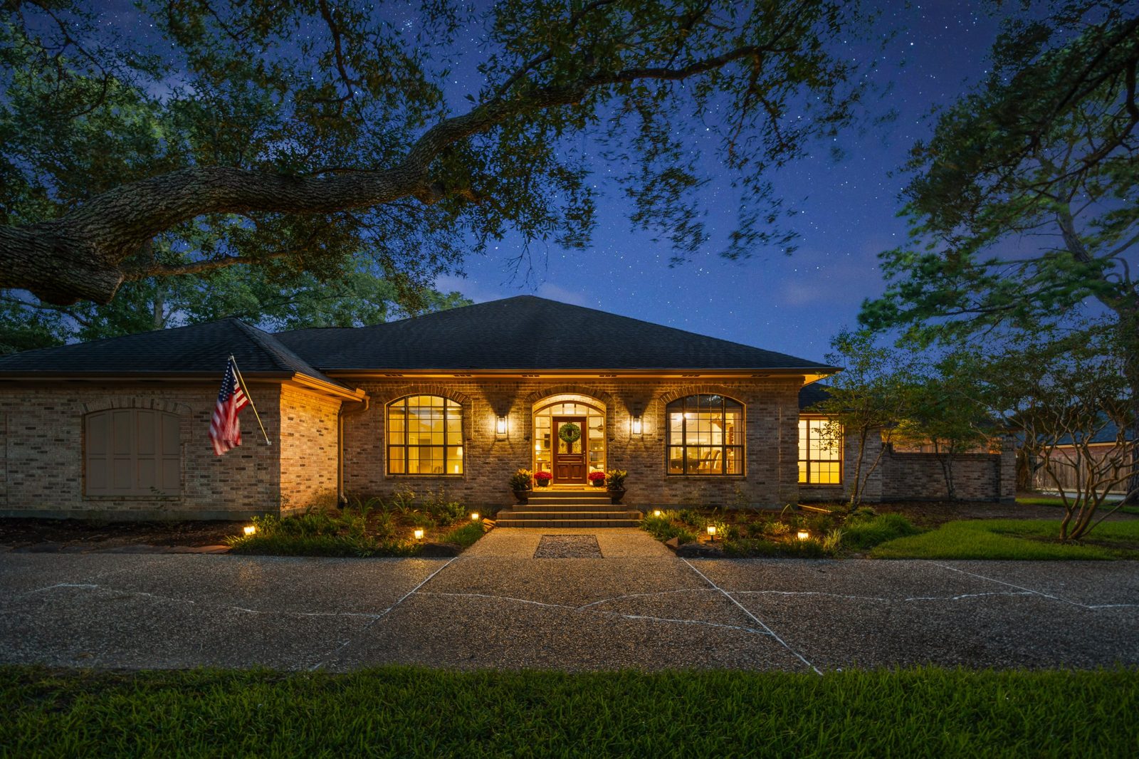 Brick home lit up at night under oak trees